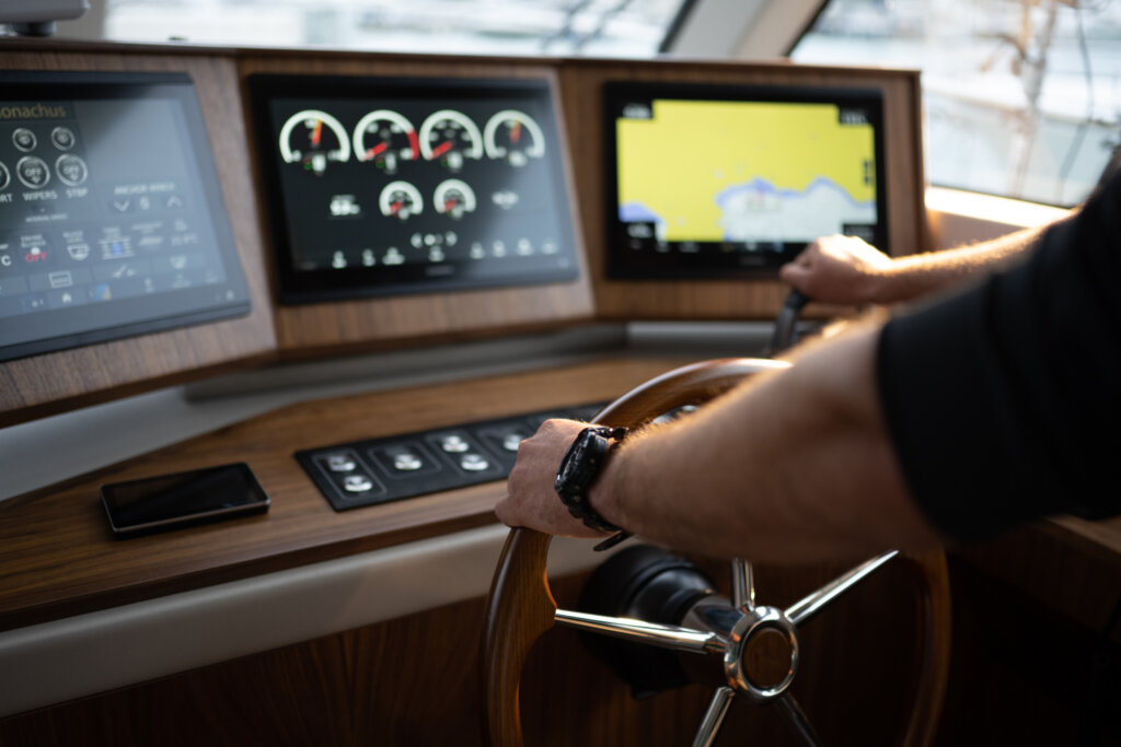 Nahaufnahme von Männerhänden, die ein Steuerrad einer Yacht bedienen.